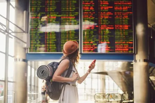 Reisende mit Rucksack vor der Anzeigetafel am Flughafen