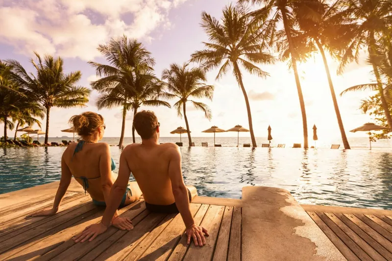 Paar blickt am Pool in den Sonnenuntergang über dem Meer